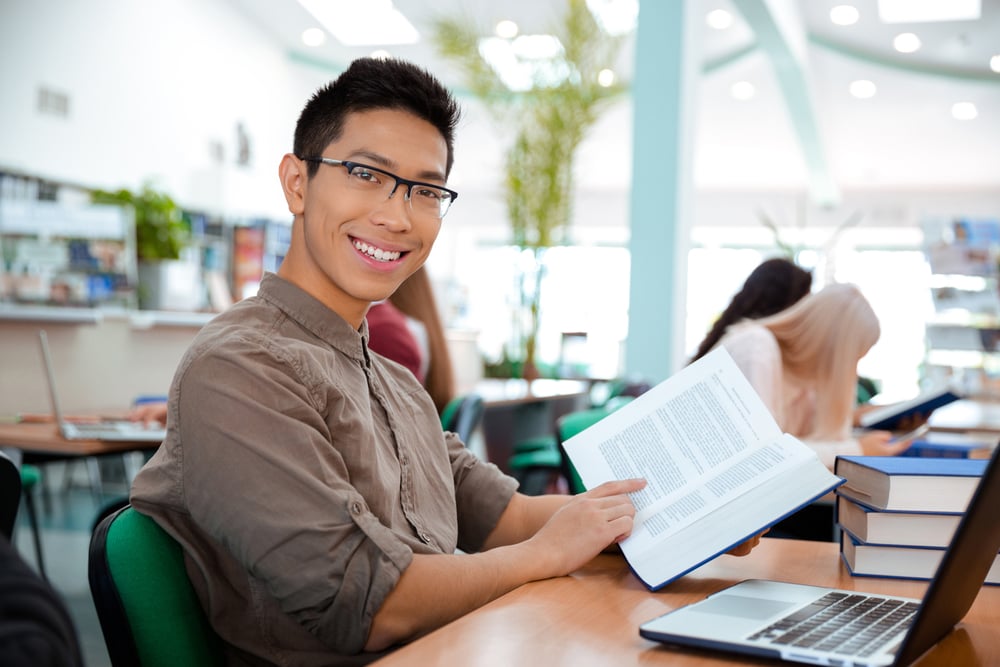 Portrait of a smiling asian man sitting at the table with book in university